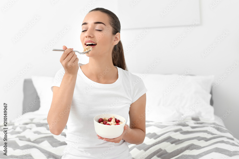 Beautiful young woman eating tasty oatmeal for breakfast in bedroom Beautiful young woman eating tasty oatmeal for breakfast in bedroom