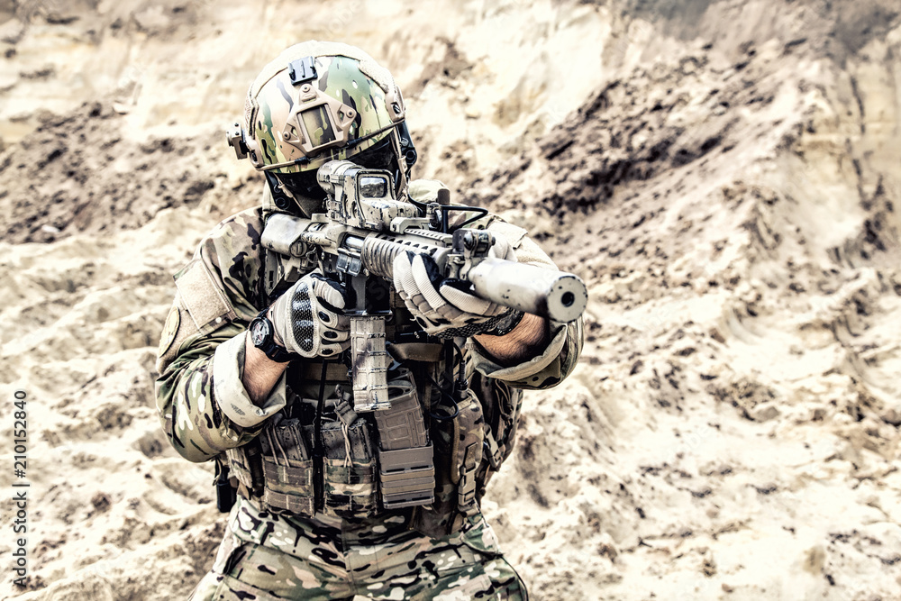 Special operations forces fighter, modern infantry soldier in full ammunition, aiming with red dot sight and shooting with assault carbine in desert area. Fire contact with enemy during war conflict Special operations forces fighter, modern infantry soldier in full ammunition, aiming with red dot sight and shooting with assault carbine in desert area. Fire contact with enemy during war conflict