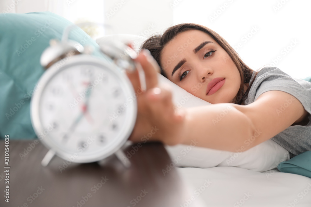 Young woman with alarm clock on bed in morning Young woman with alarm clock on bed in morning