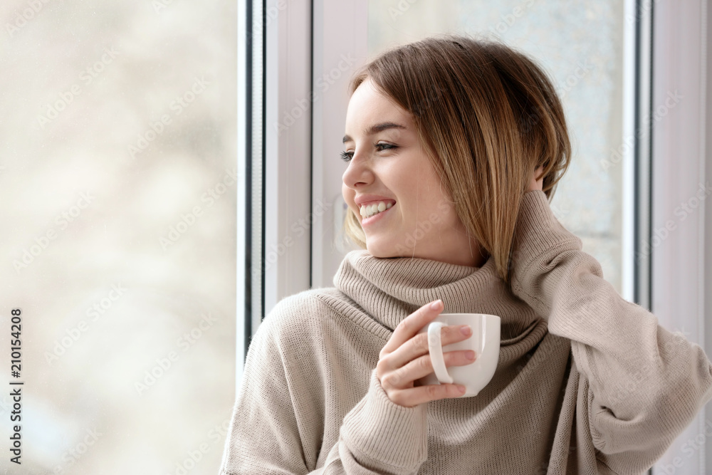 Morning of beautiful young woman drinking hot coffee near window Morning of beautiful young woman drinking hot coffee near window