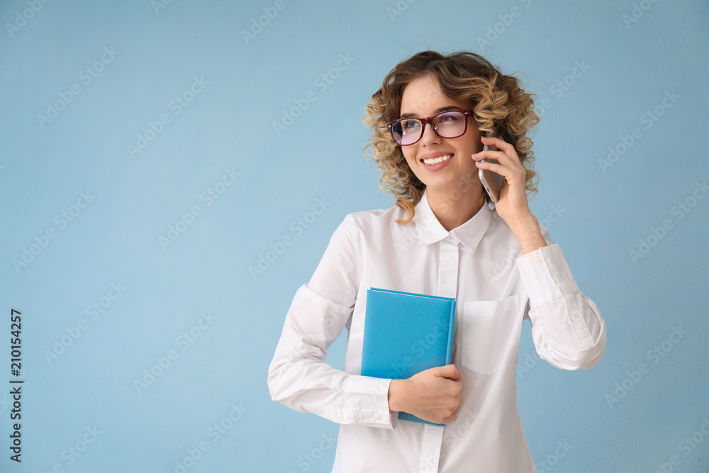 Beautiful young woman in formal clothes talking by mobile phone on color background