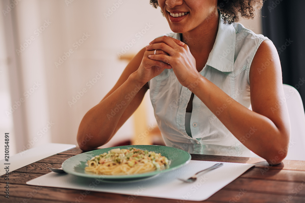 Beautiful mixed race woman eating pasta for dinner while sitting at kitchen table. Beautiful mixed race woman eating pasta for dinner while sitting at kitchen table.