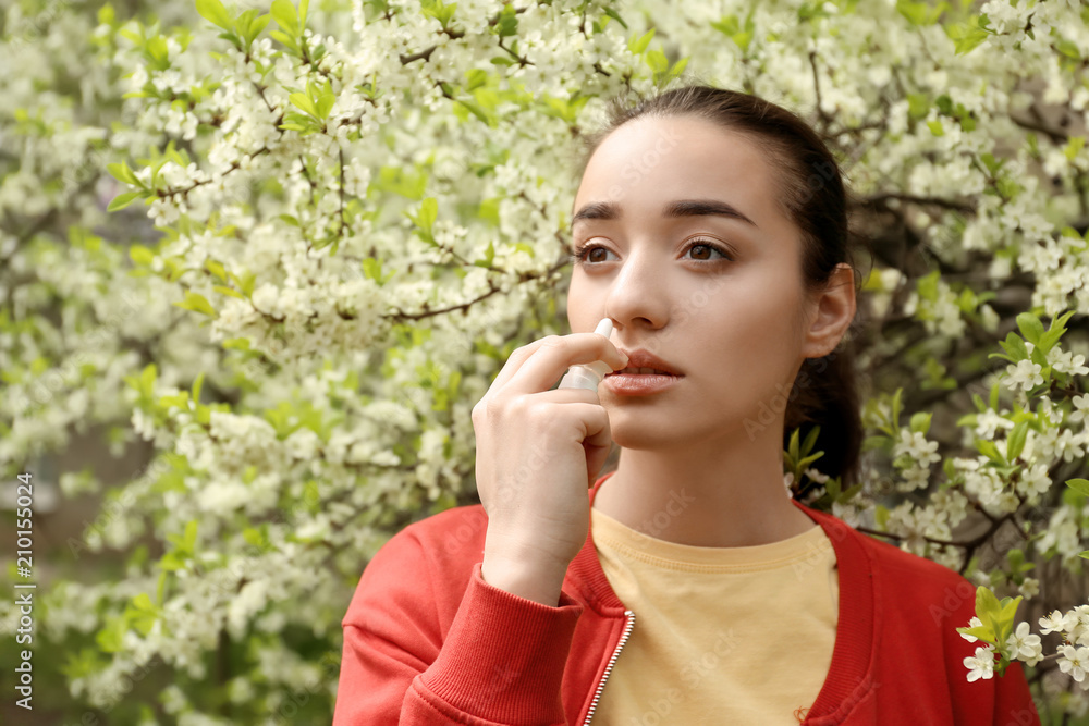 Young woman using nasal drops near blooming tree. Allergy concept Young woman using nasal drops near blooming tree. Allergy concept