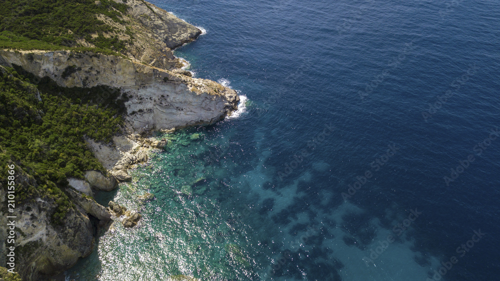 Aerial view of a rocky coastline overlooking the Mediterranean Sea. On the mountain grows a forest with many trees and there is some big rock in the blue and azure sea.