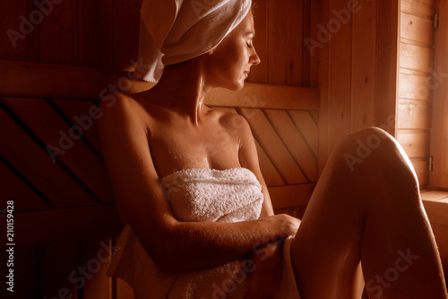 girl in a spa treatment in a traditional sauna with a brush for skin and a washcloth. relaxes wrapped in a white towel photo