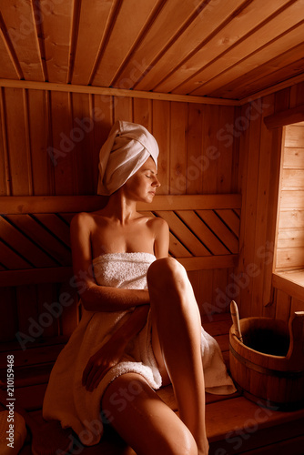 girl in a spa treatment in a traditional sauna with a brush for skin and a washcloth. relaxes wrapped in a white towel photo