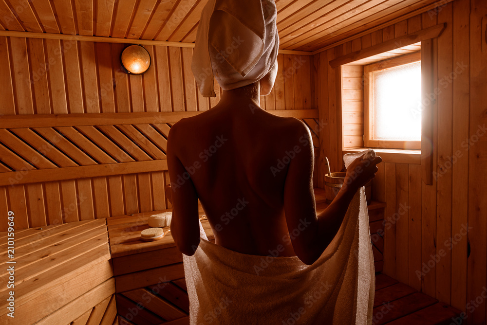 girl in a spa treatment in a traditional sauna with a brush for skin and a washcloth. relaxes wrapped in a white towel