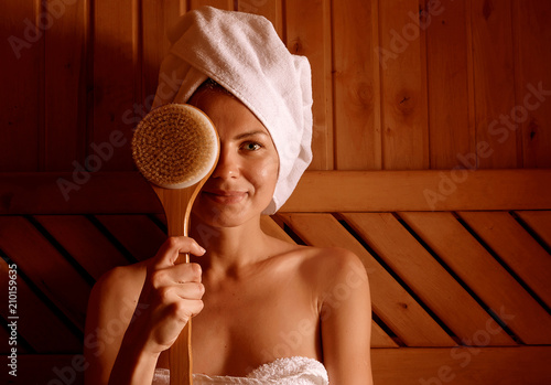 girl in a spa treatment in a traditional sauna with a brush for skin and a washcloth. relaxes wrapped in a white towel photo