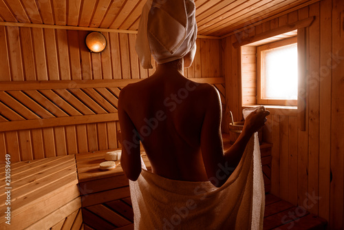 Obraz na płótnie girl in a spa treatment in a traditional sauna with a brush for skin and a washcloth. relaxes wrapped in a white towel w salonie