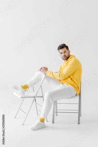 attractive young man in yellow hoodie sitting on chairs on white