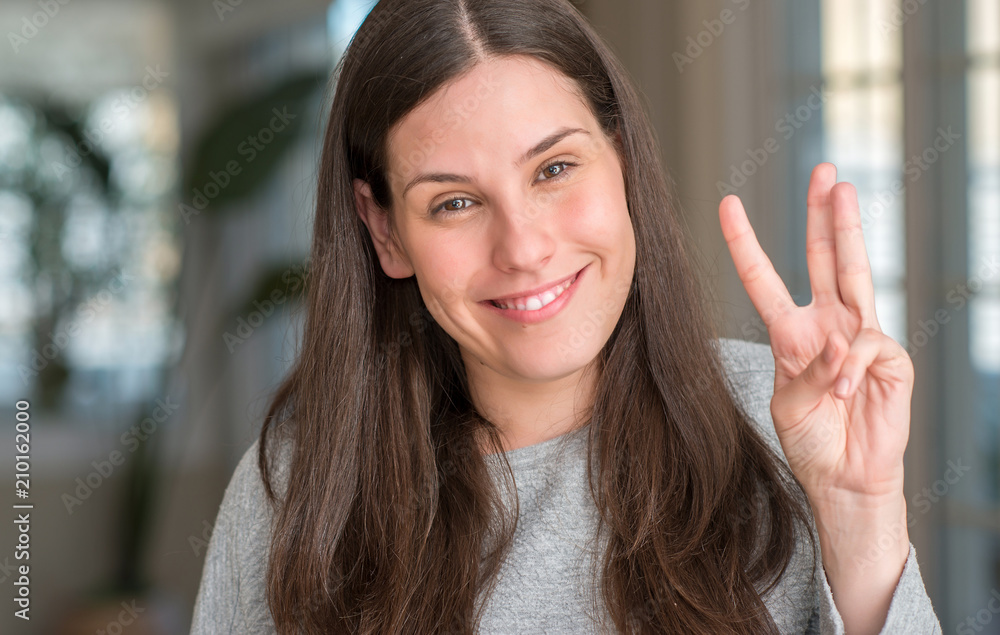 Young beautiful woman at home showing and pointing up with fingers number three while smiling confident and happy.