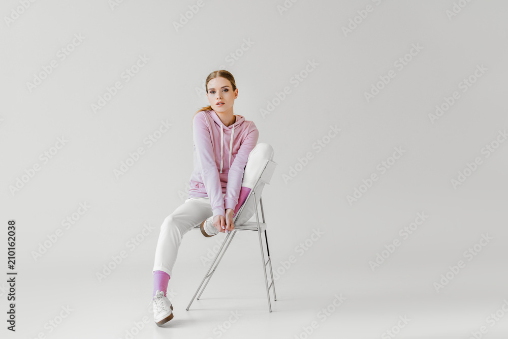 beautiful young woman in pink hoodie sitting on chair on white and looking at camera beautiful young woman in pink hoodie sitting on chair on white and looking at camera