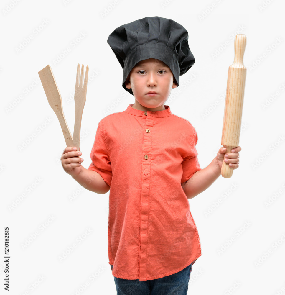 Dark haired little child wearing chef uniform with a confident expression on smart face thinking serious Dark haired little child wearing chef uniform with a confident expression on smart face thinking serious