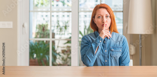 Redhead woman at home asking to be quiet with finger on lips. Silence and secret concept.