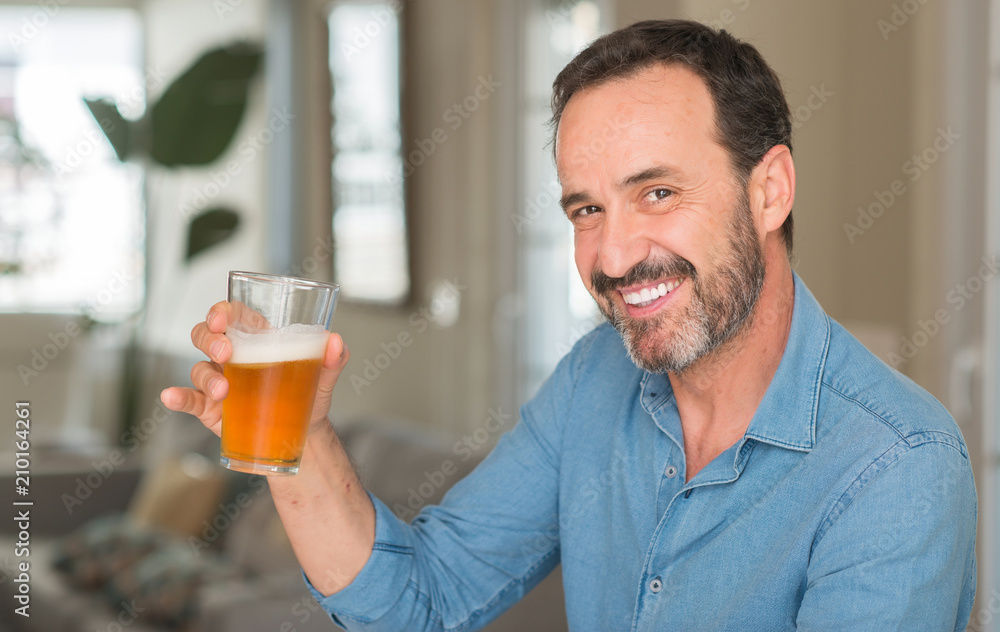 Middle age man drinking beer with a happy face standing and smiling with a confident smile showing teeth Middle age man drinking beer with a happy face standing and smiling with a confident smile showing teeth