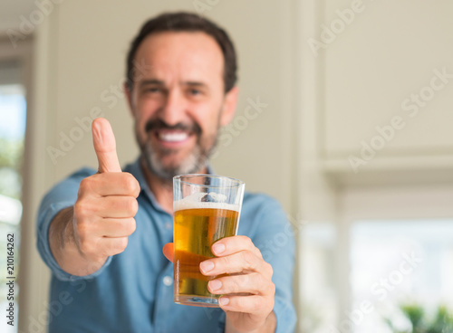 Middle age man drinking beer happy with big smile doing ok sign, thumb up with fingers, excellent sign