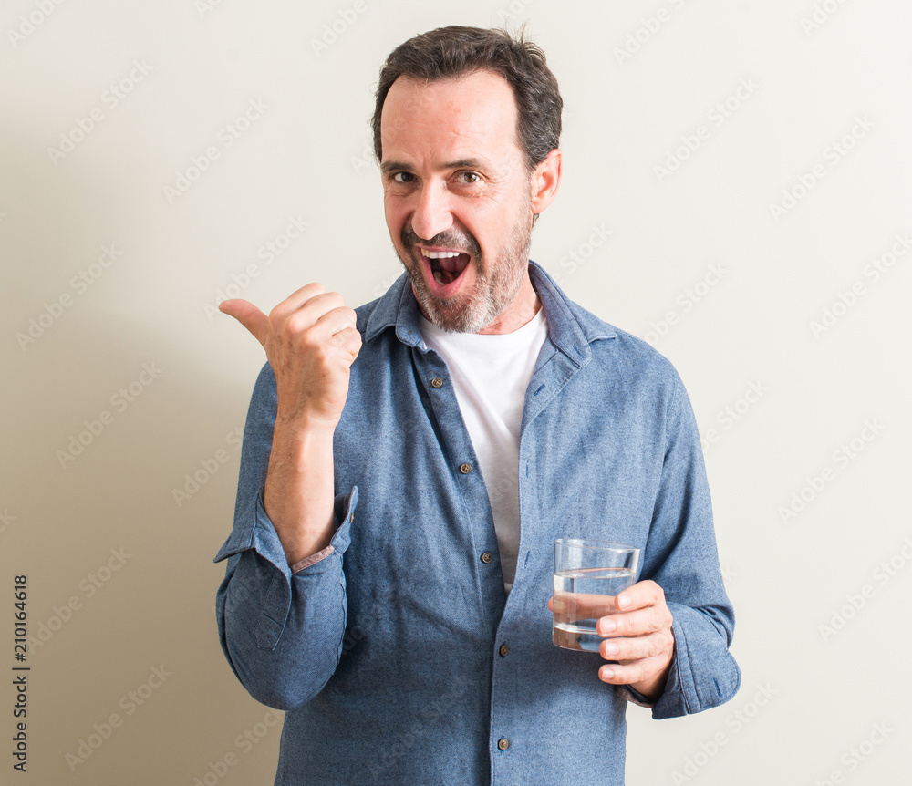 Senior man drinking water in a glass pointing with hand and finger up with happy face smiling Senior man drinking water in a glass pointing with hand and finger up with happy face smiling