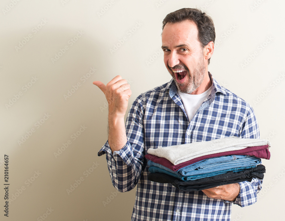 Senior man holding folded laundry clothes pointing with hand and finger up with happy face smiling