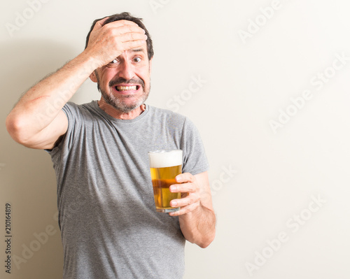 Senior man drinking beer stressed with hand on head, shocked with shame and surprise face, angry and frustrated. Fear and upset for mistake.