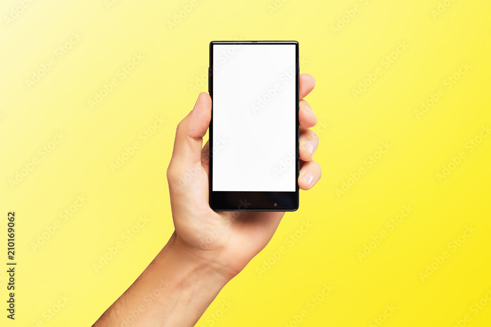 Mockup of male hand holding black frameless cell phone with blank screen isolated at yellow background. Mockup of male hand holding black frameless cell phone with blank screen isolated at yellow background.