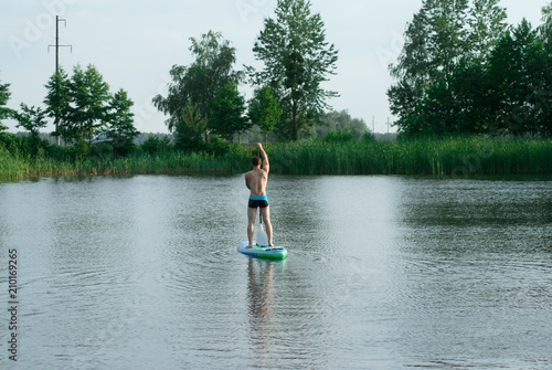 A man stands on a SAP Board with an oar and swims through a forest lake,