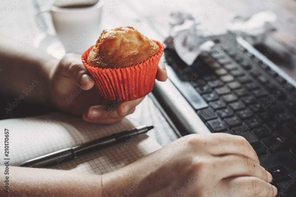 Unhealthy snack at work time. Woman eating muffin at workplace. High