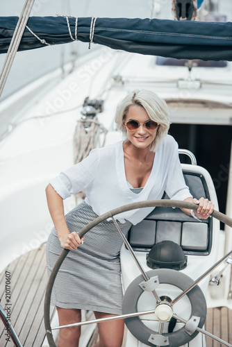 beautiful smiling girl in sunglasses standing at steering wheel on yacht © LIGHTFIELD STUDIOS