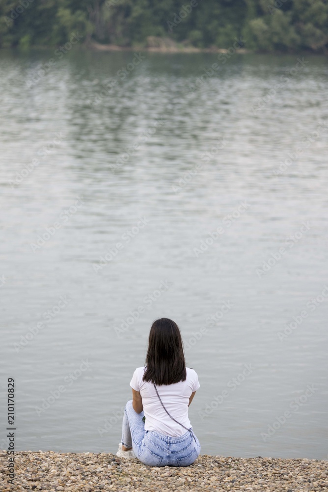 girl from behind sitting on river beach