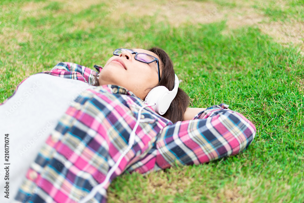 Beautiful women in colorful plaid shirt laying down on green grass happliy listening music Beautiful women in colorful plaid shirt laying down on green grass happliy listening music