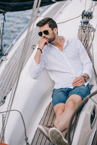 High angle view of pensive young man in sunglasses looking away while sitting on yacht © LIGHTFIELD STUDIOS