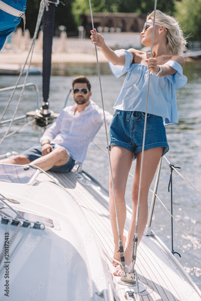 young man in sunglasses sitting and looking at beautiful girl on yacht