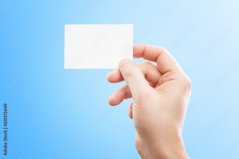 Obraz premium Male hand holding white business card at isolated blue background mockup.