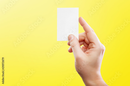 Male hand holding white business card at isolated yellow background mockup.