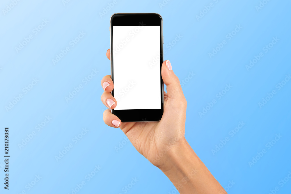 Female hand holding black cellphone with white screen at isolated blue background.
