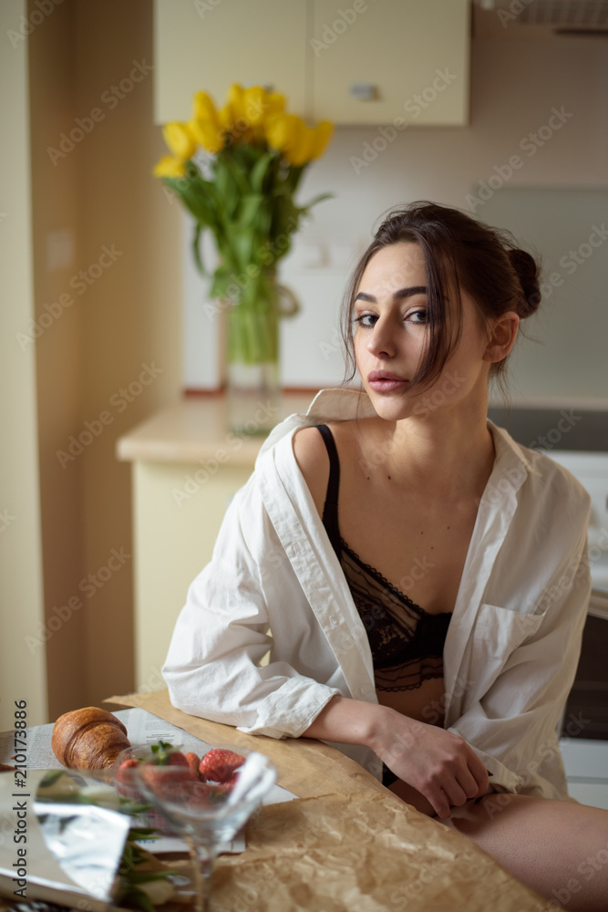 beautiful young girl in lingerie having breakfast with croissant in the kitchen beautiful young girl in lingerie having breakfast with croissant in the kitchen