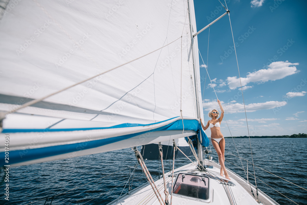 Obraz premium distant view of attractive young woman in swimwear standing on yacht