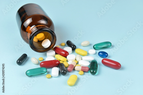 Assorted medicine pills pouring out of the brown bottle on blue background.