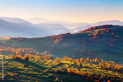 Extraordinary autumn scenery. Green fields with haystacks. Trees covered with orange and crimson leaves. Mountain landscapes. Nice rays of the sun. Location place Ukrain, Europe.