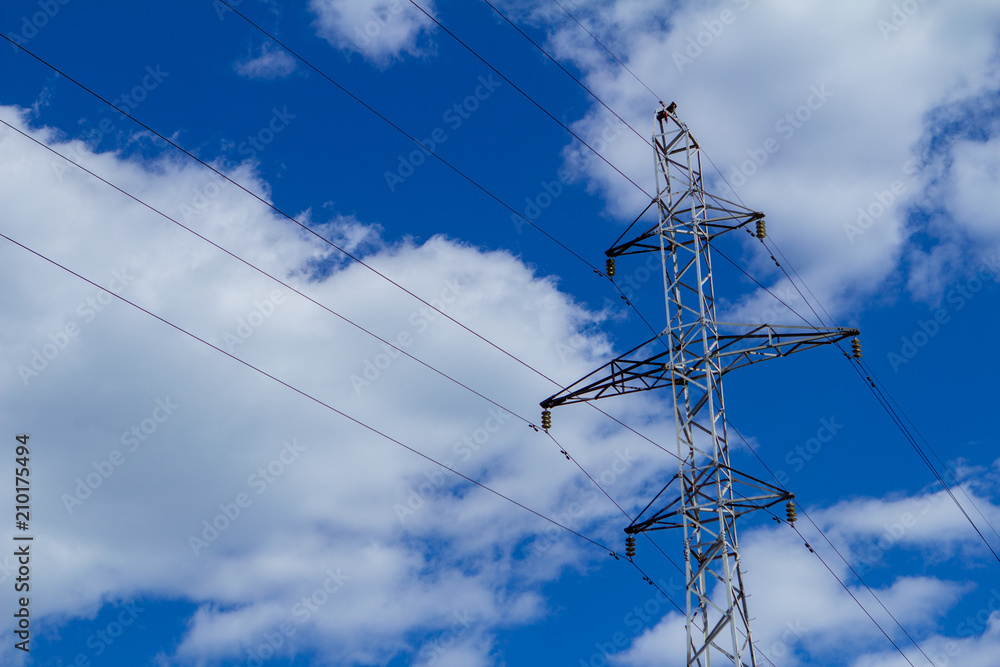 Electric high voltage tower with electric line against clouds blue sky