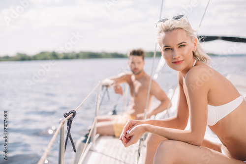 selective focus of young attractive woman in bikini and her boyfriend sitting behind on yacht © LIGHTFIELD STUDIOS