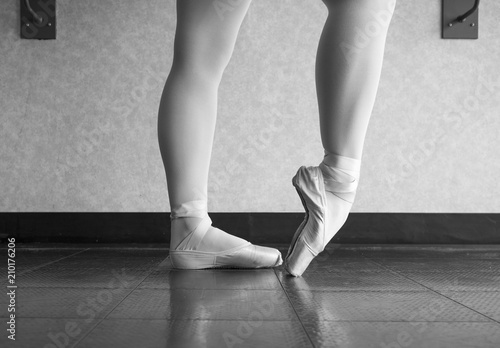 Black and white version of ballet dancer warming up her feet in her pointe shoes for ballet class