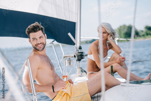 smiling couple in swimwear relaxing with champagne glasses on yacht