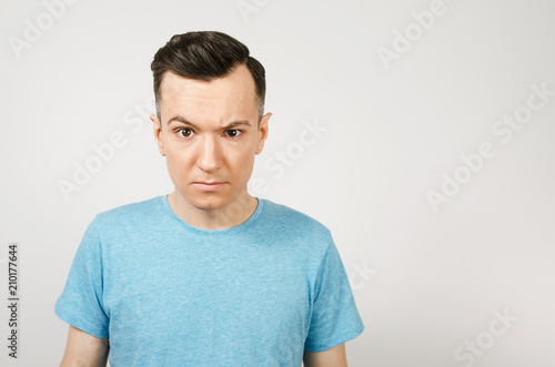 Obraz na plátně Young gloomy man dressed in a blue t-shirt on a light background.