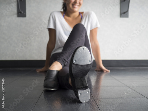 Smiling teenage tap dancer sitting cross legged in dance class relaxing  photo