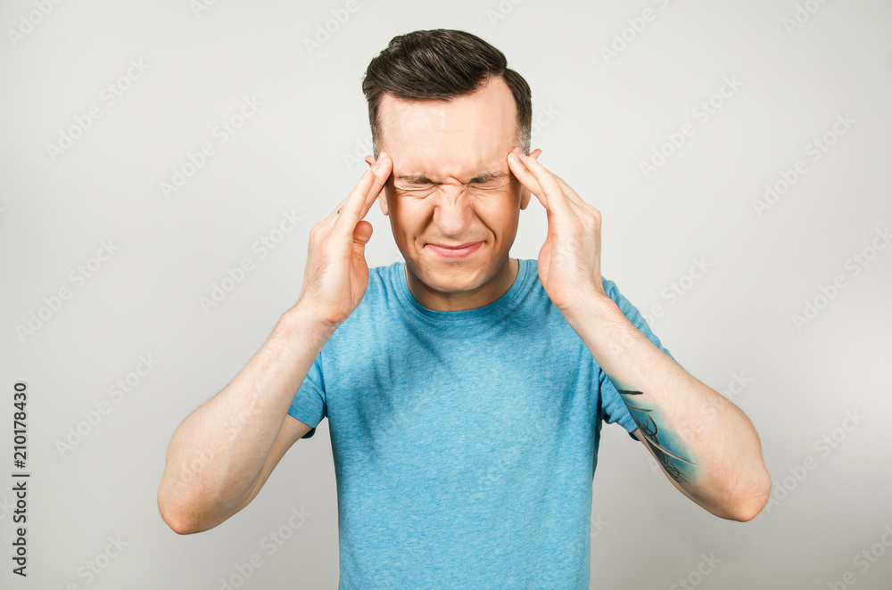 Young guy with headache dressed in a blue t-shirt on a light background. Young guy with headache dressed in a blue t-shirt on a light background.