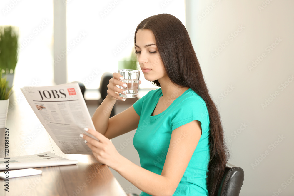 Young woman reading newspaper while drinking water in cafe