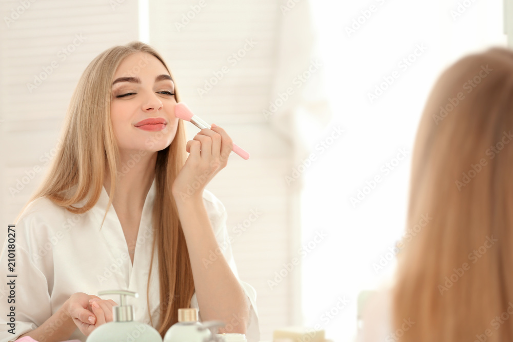 Young woman applying makeup in bathroom