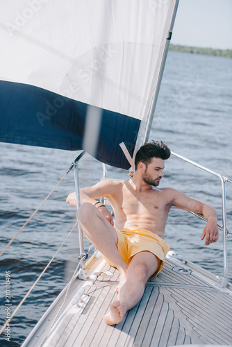 Fényképezés shirtless muscular man in swim trunks having sunbath on yacht