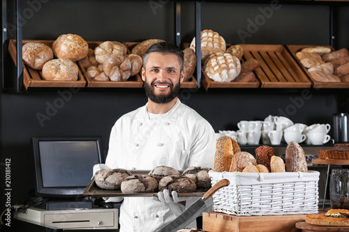 Male baker holding tray with fresh bread in shop