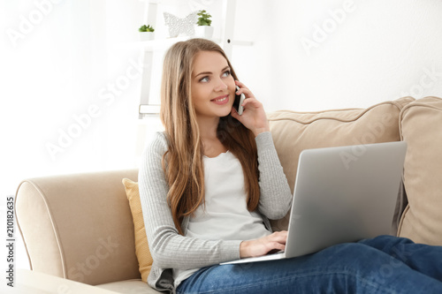 Female freelancer talking by phone while working on laptop at home